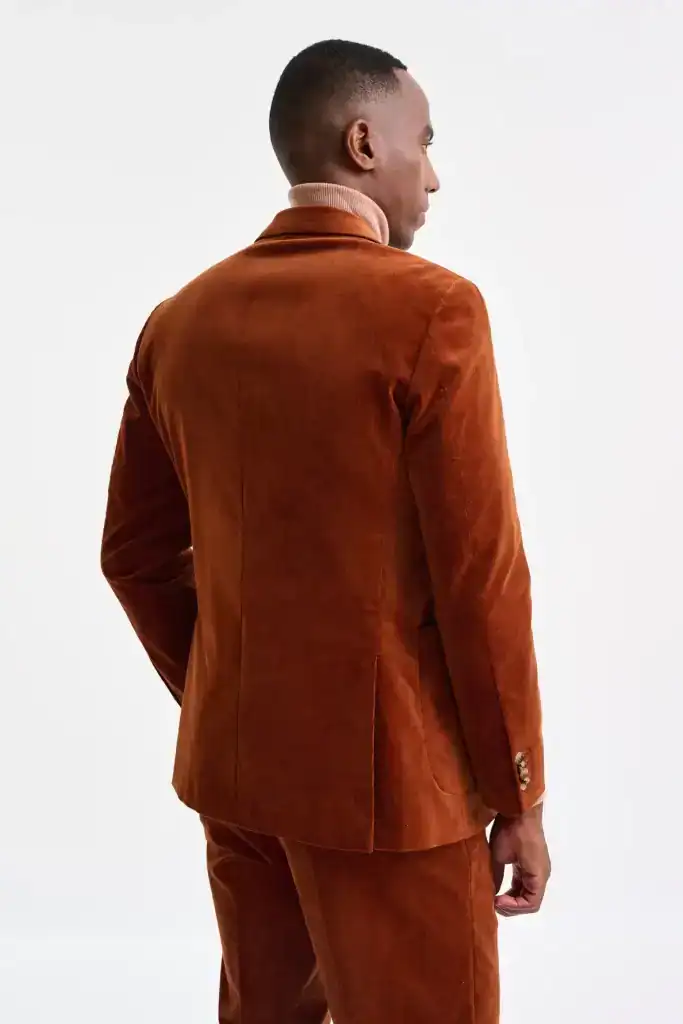 Elegante hombre con traje de pana color marrón, de espaldas, en un fondo blanco, modelo en una sesión de moda, resaltando estilo y sofisticación, para contenido de moda masculina.